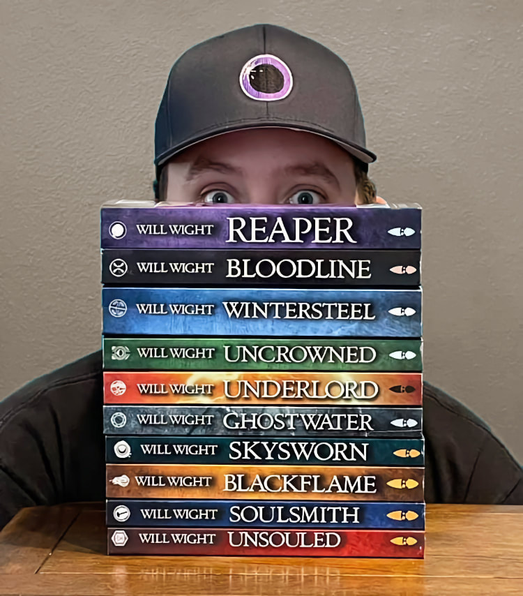 Porttrait of Will Wight, hiding his face behind a stack of his books